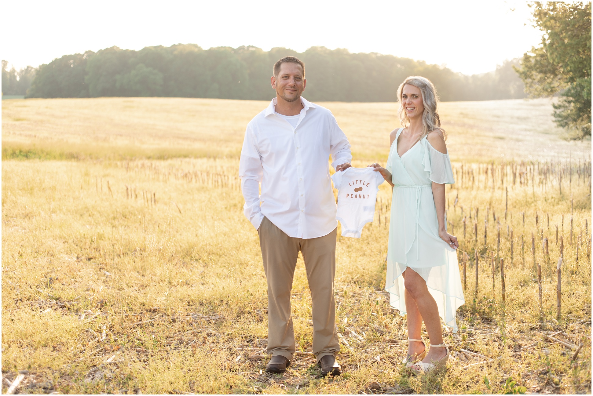 Husband and Wife holding a onesie in the field with golden light