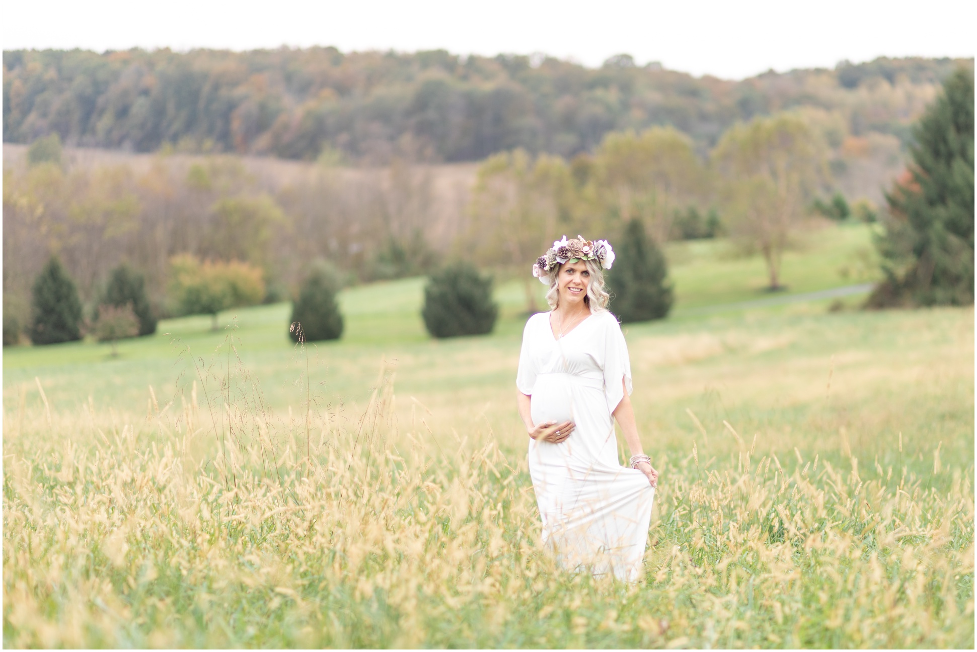 Rebecca standing in the middle of an open field for her maternity session in a white dress and a fall flower crown
