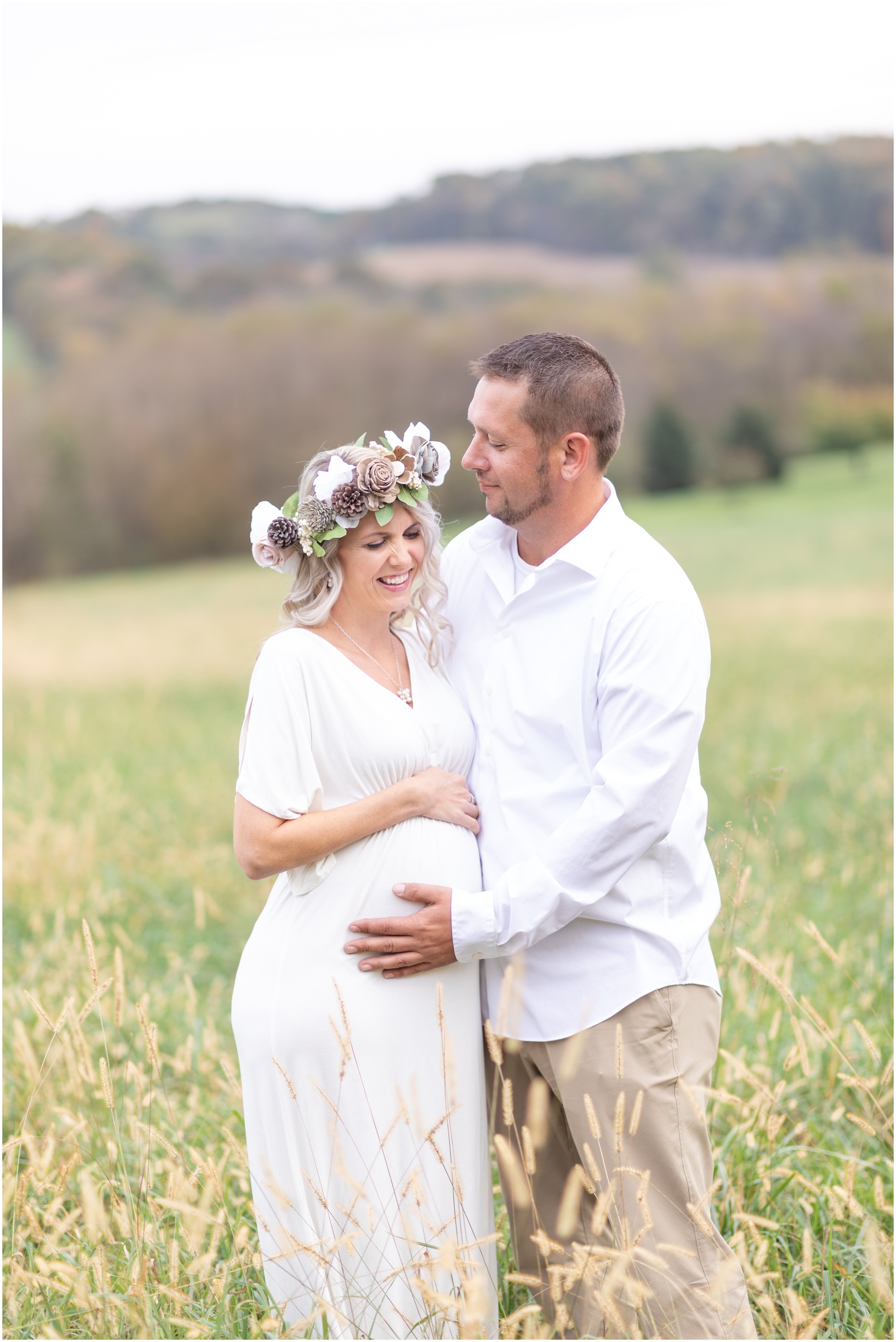 Rebecca and Scott in the field for their maternity session. Rebecca in a white dress with a fall flower crown.