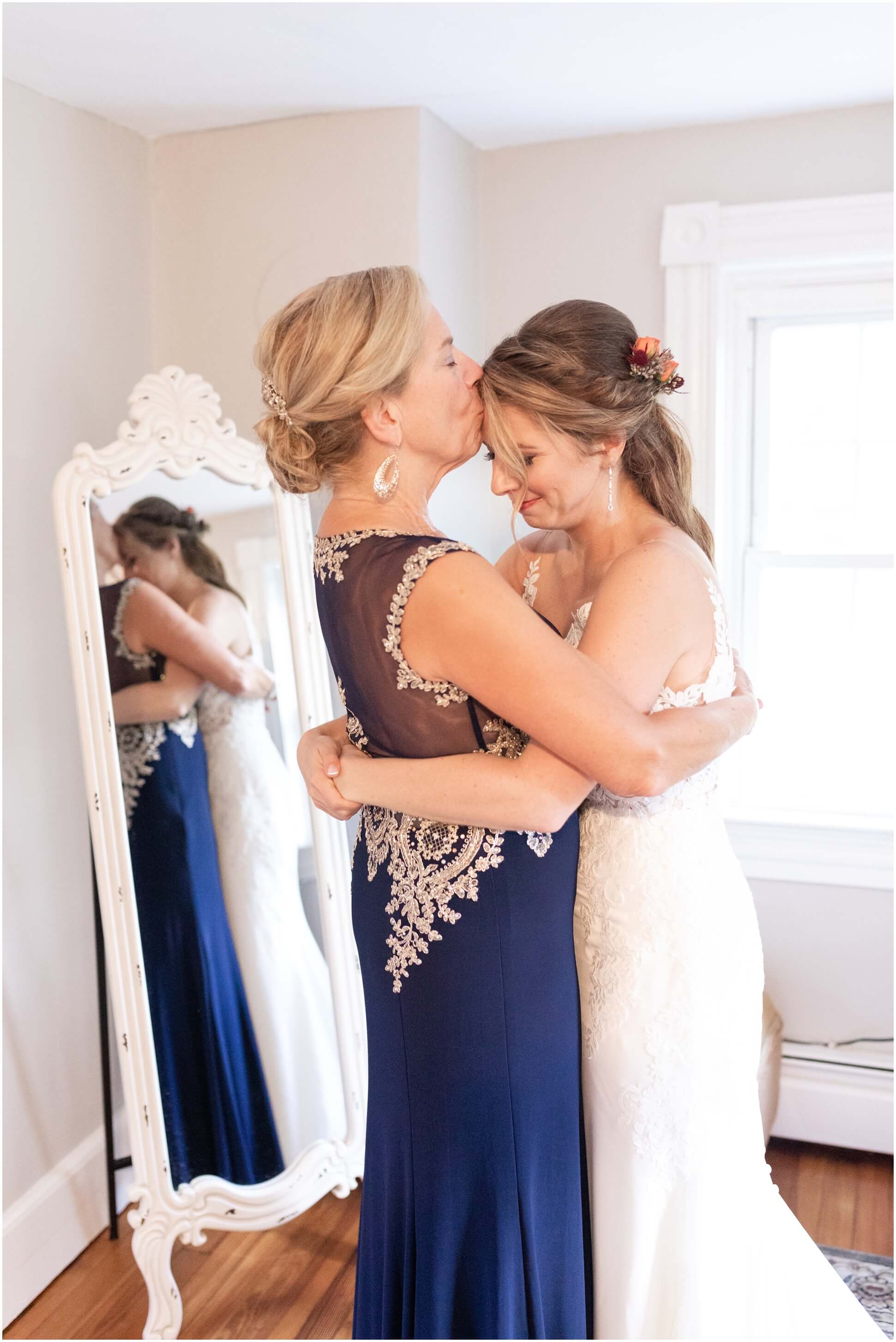 MOTHER OF THE BRIDE KISSING BRIDE ON THE FOREHEAD IN THE BRIDAL SUITE