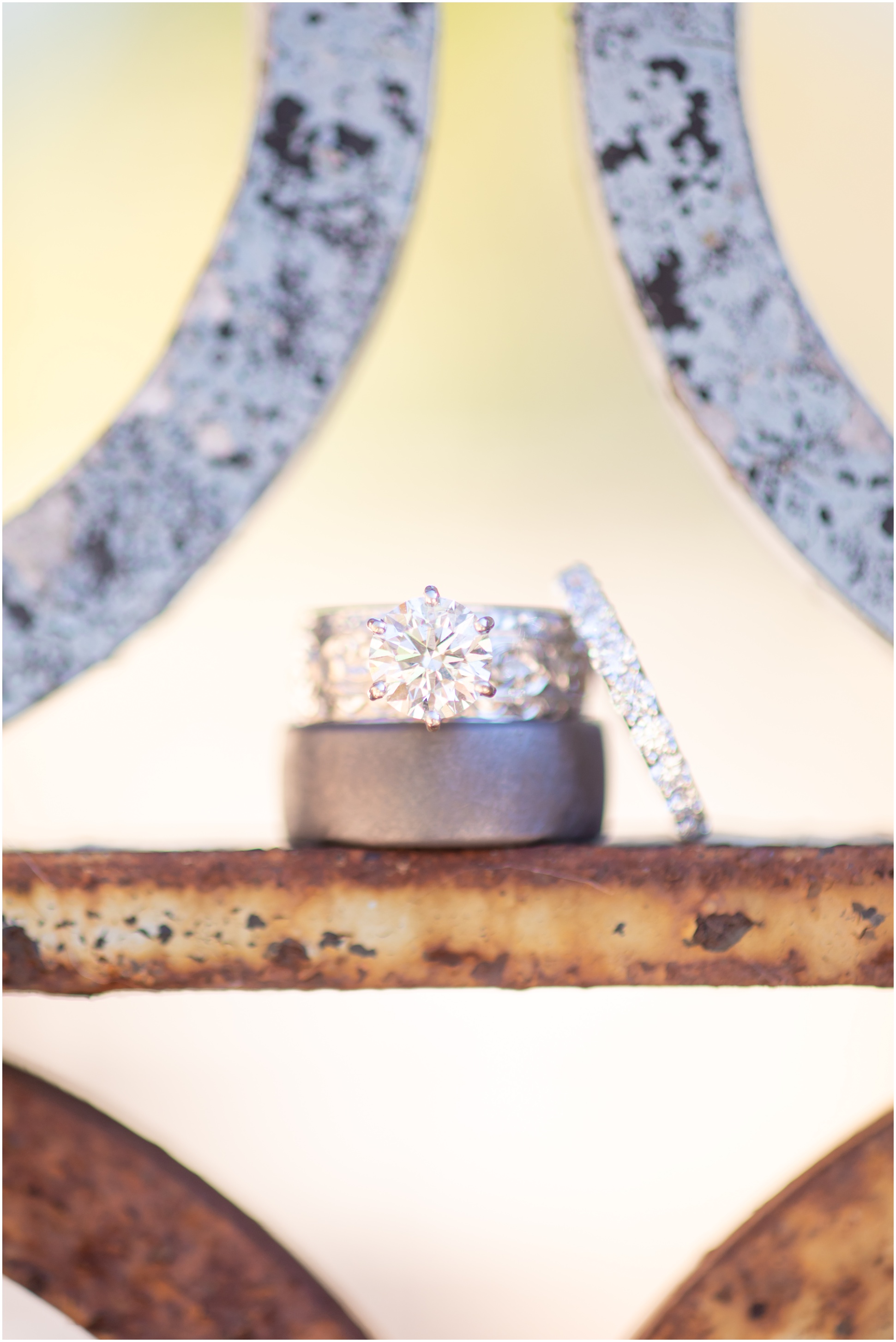 Round Cut 1 Carat Diamond Engagement Ring, a wedding band, and a groom's wedding band stacked on a fence