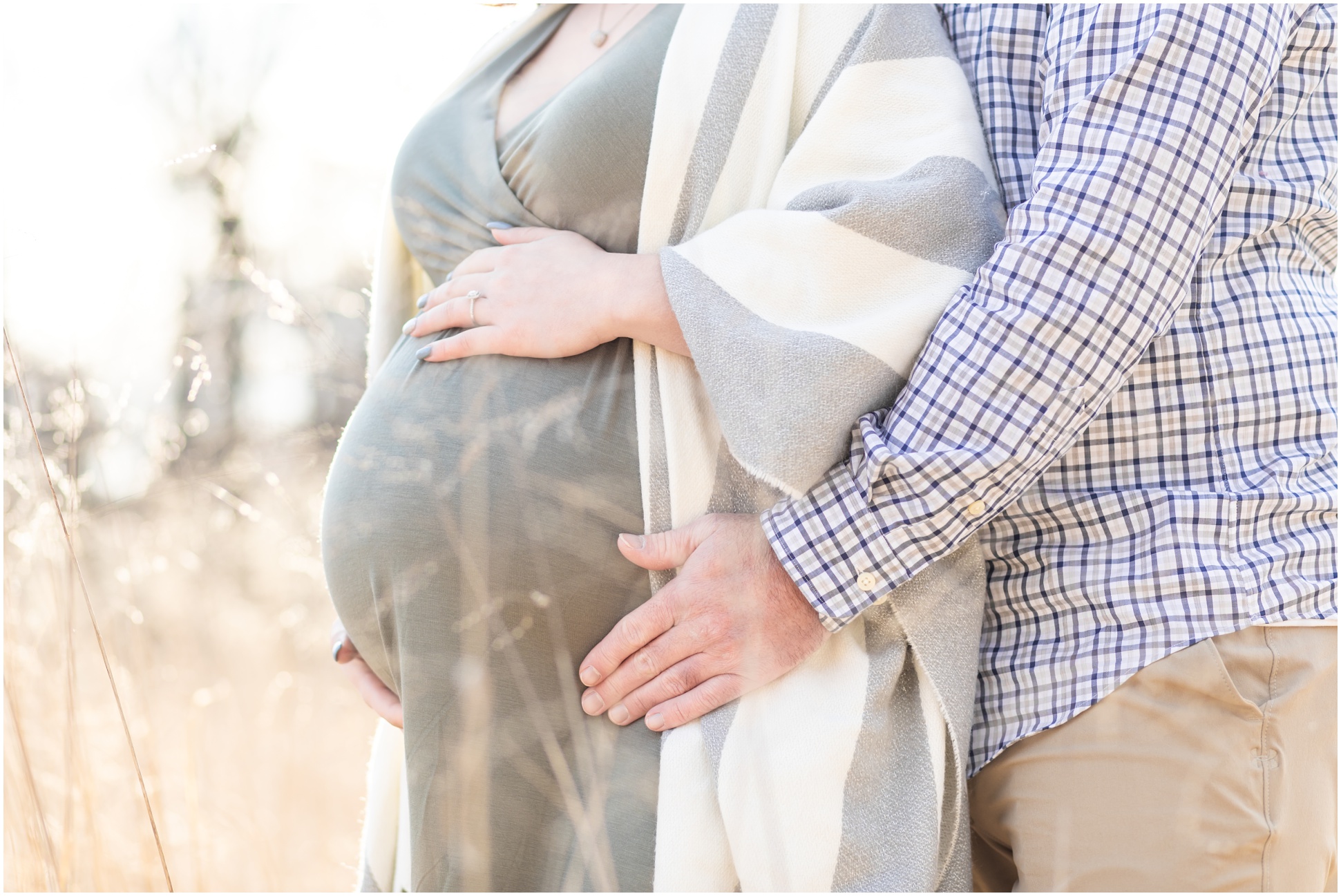 Close up of dad and mom-to-be snuggling their baby bump in a field of tall golden grass