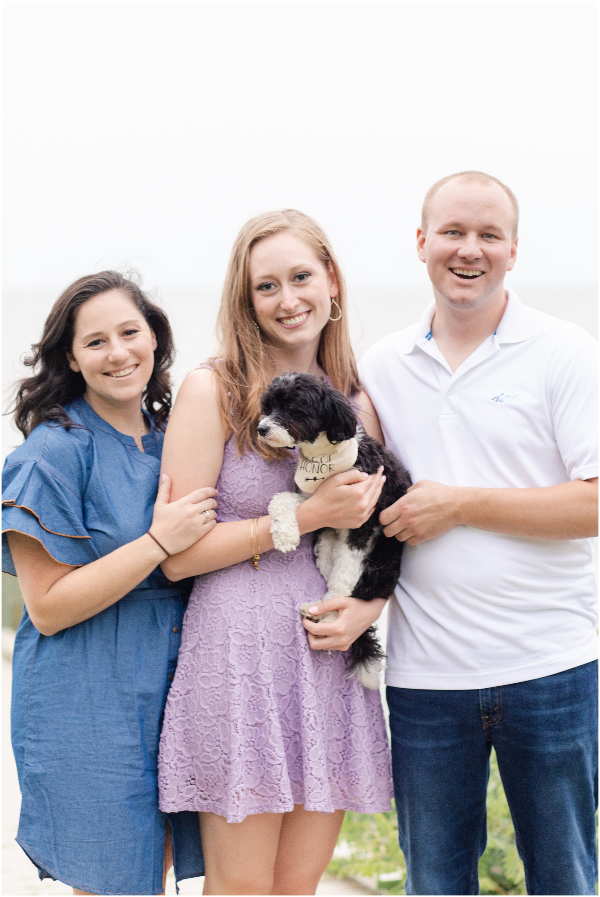 Maid of Honor, Groom, Bride, and their Puppy at their engagement session, smiling toward the camera