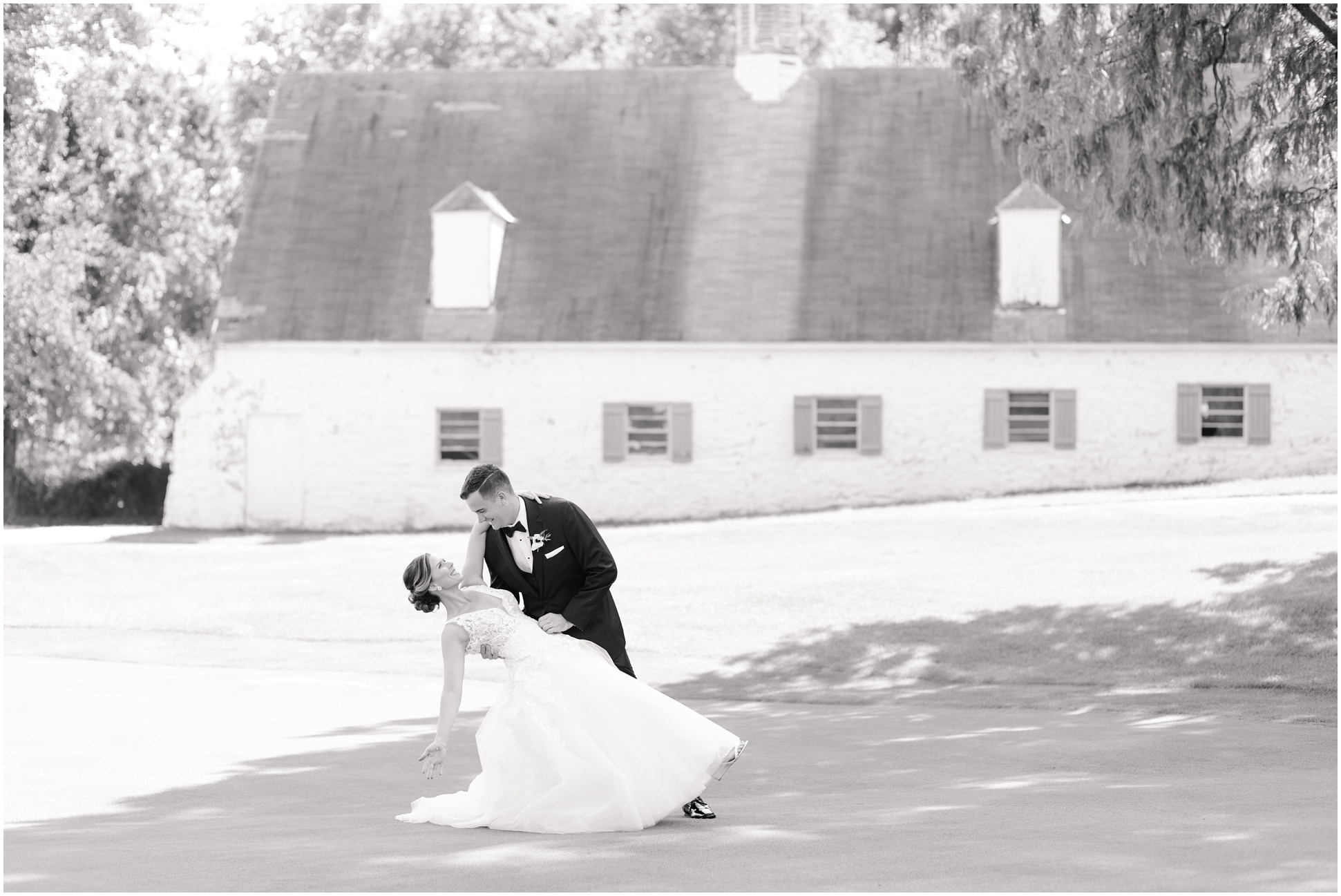 The groom dipping his bride in front of the white barn on the golf course at Eagles Nest Country Club