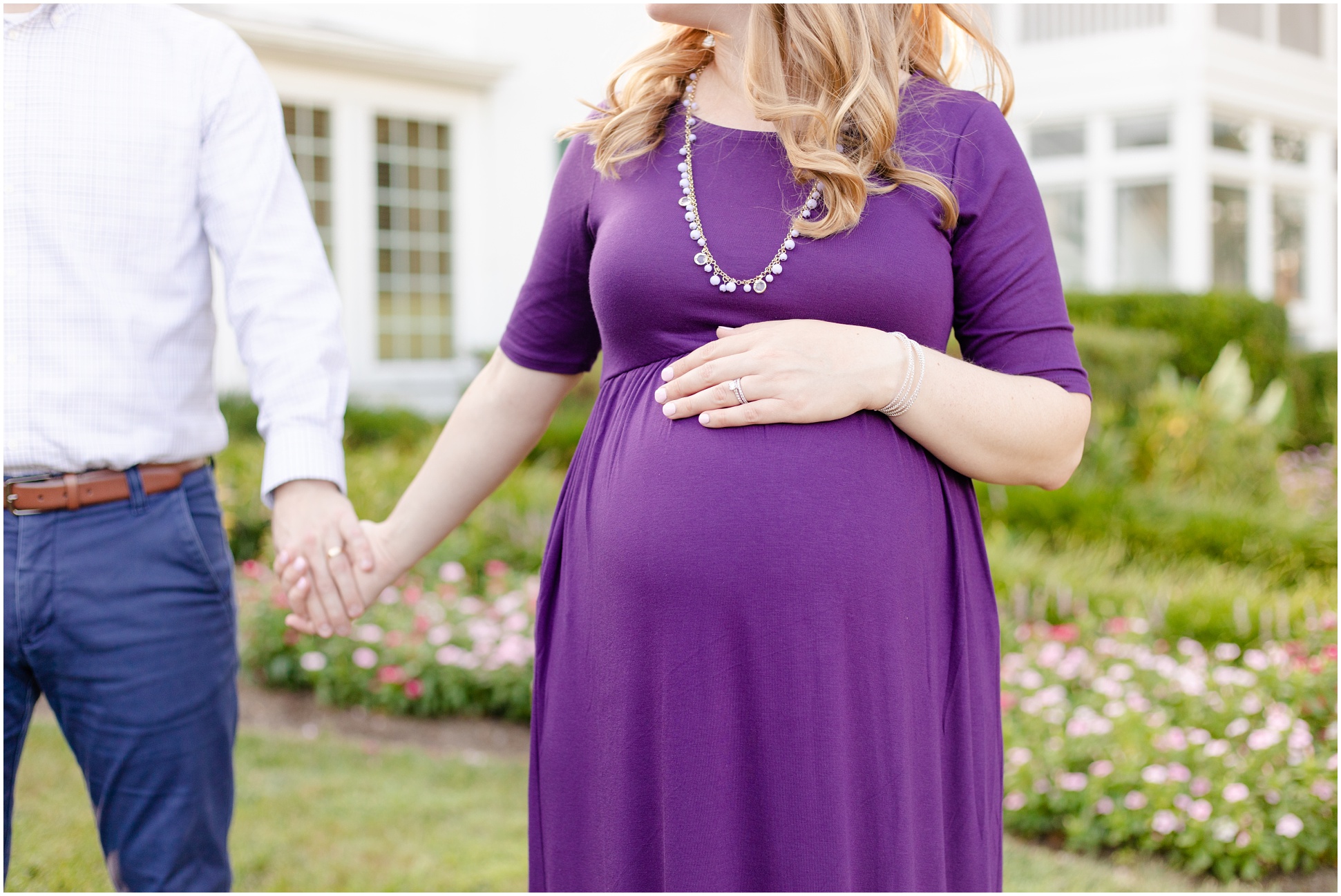 Pregnant mom wearing a purple maternity dress, beaded necklace, and her hand on her baby bump