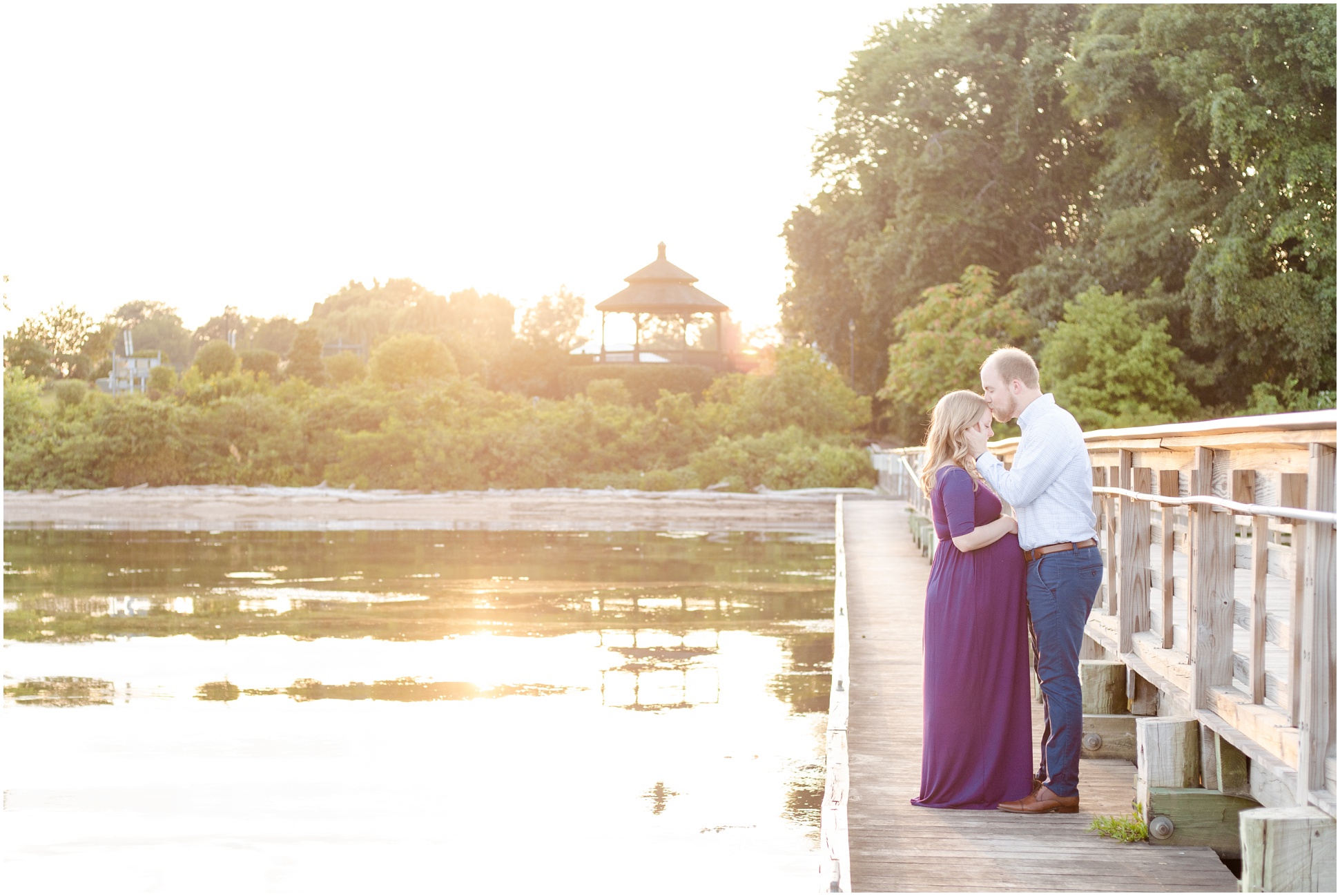 The sun setting behind the arbor on the dock of Swan Harbor Farm, as a pregnant couple kisses