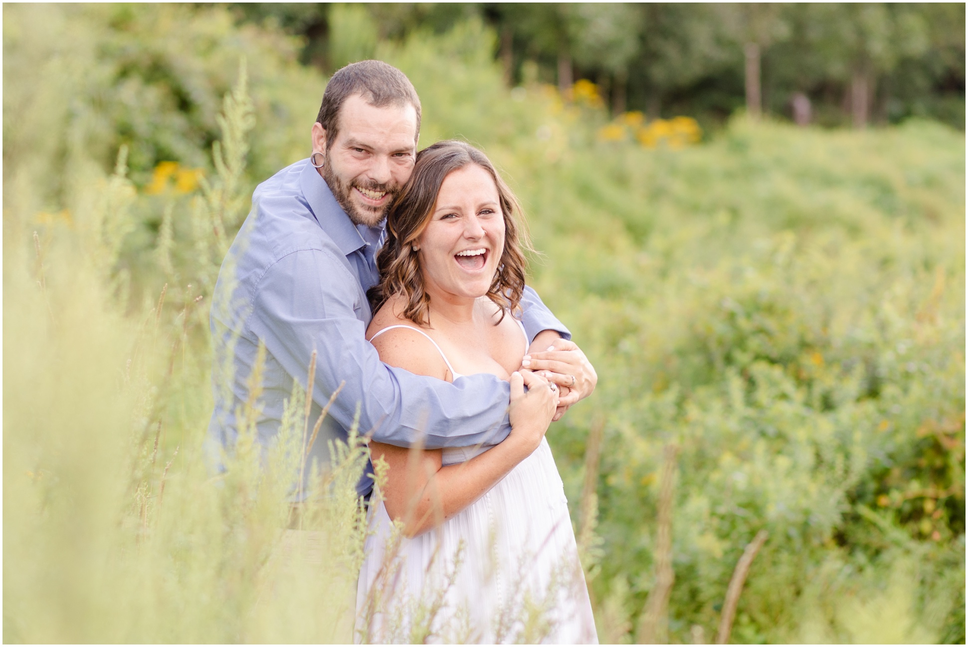 Mallory, wearing a white dress, being held by her husband Jimmy behind the tall grasses