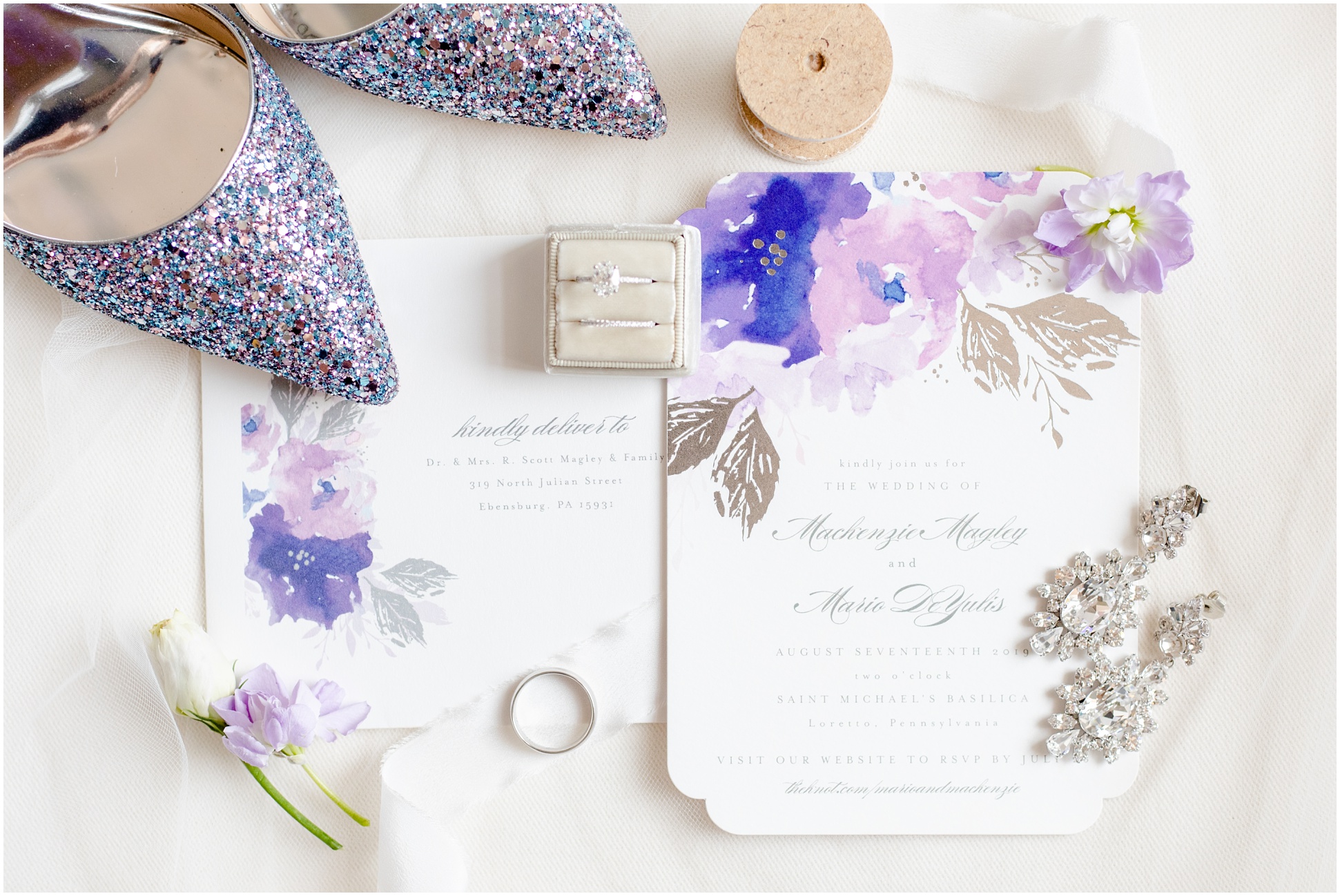 Purple sparkling stillettos, ring in ring box, purple floral invitation suite, and more in a flat lay