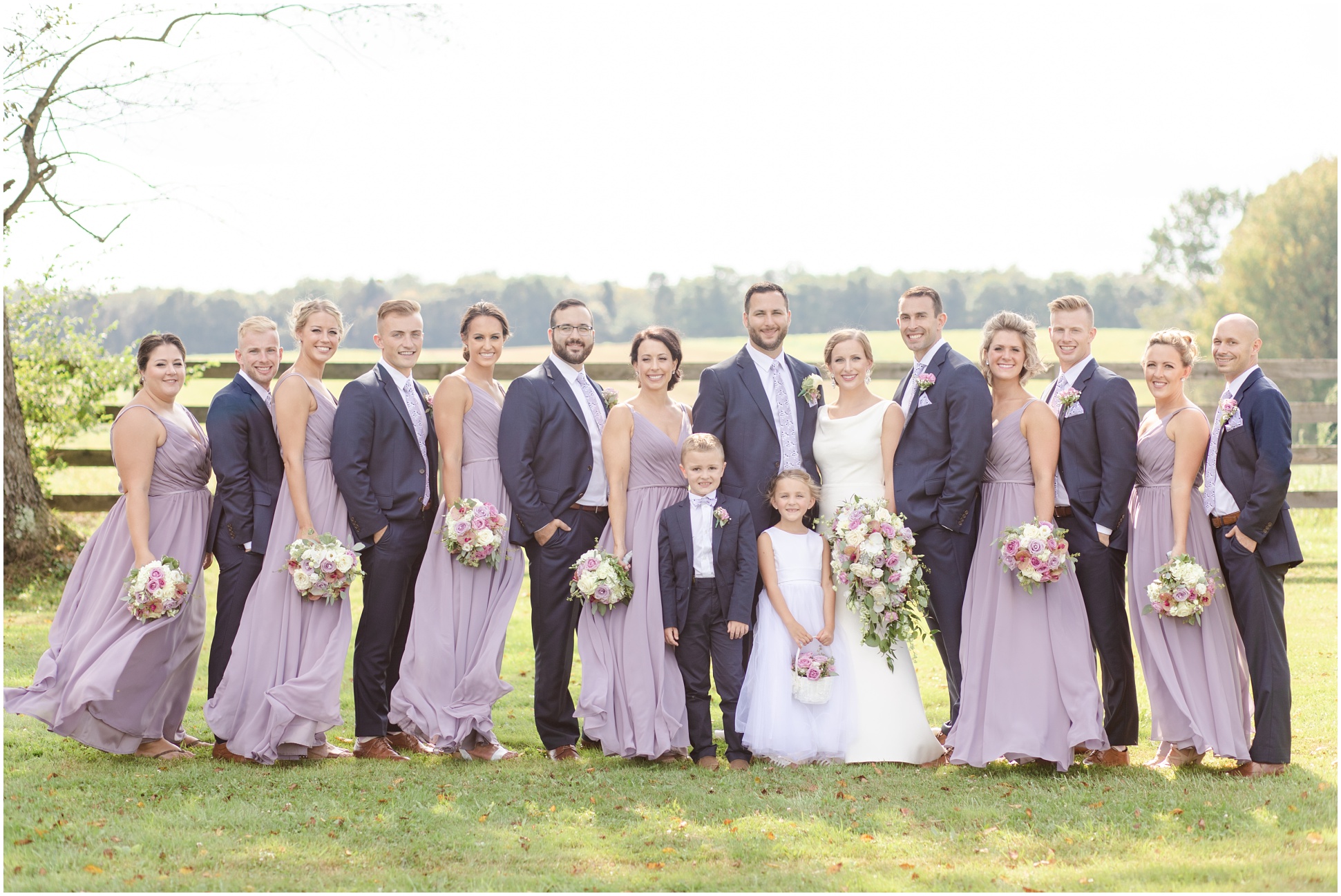 Full bridal party. Bridesmaids wearing long purple dresses, groomsmen wearing blue suits