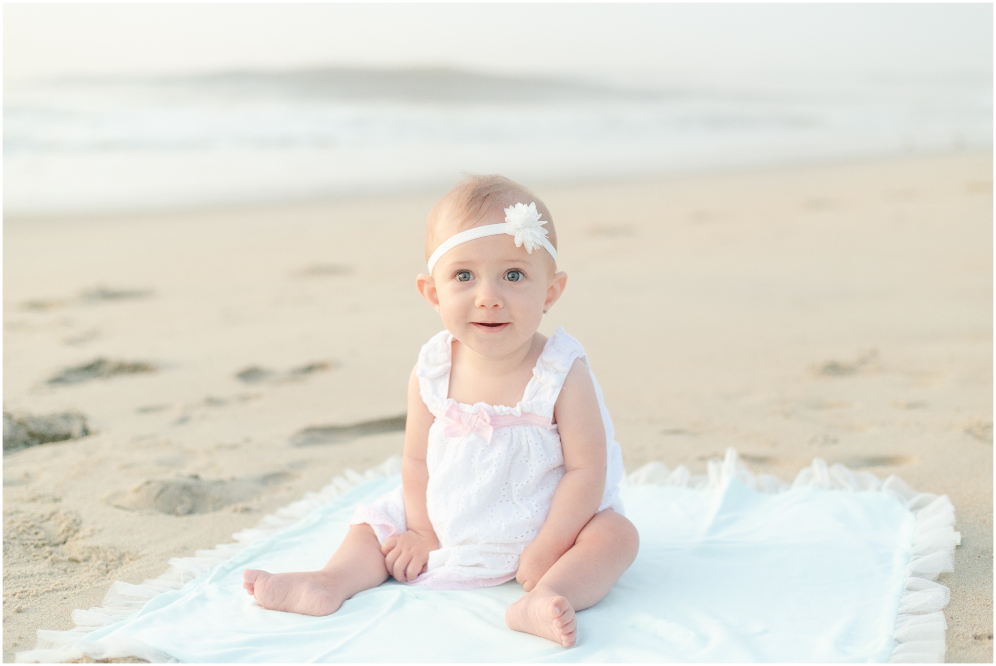 Baby Girl with white hand band sitting on a blanket in the sand
