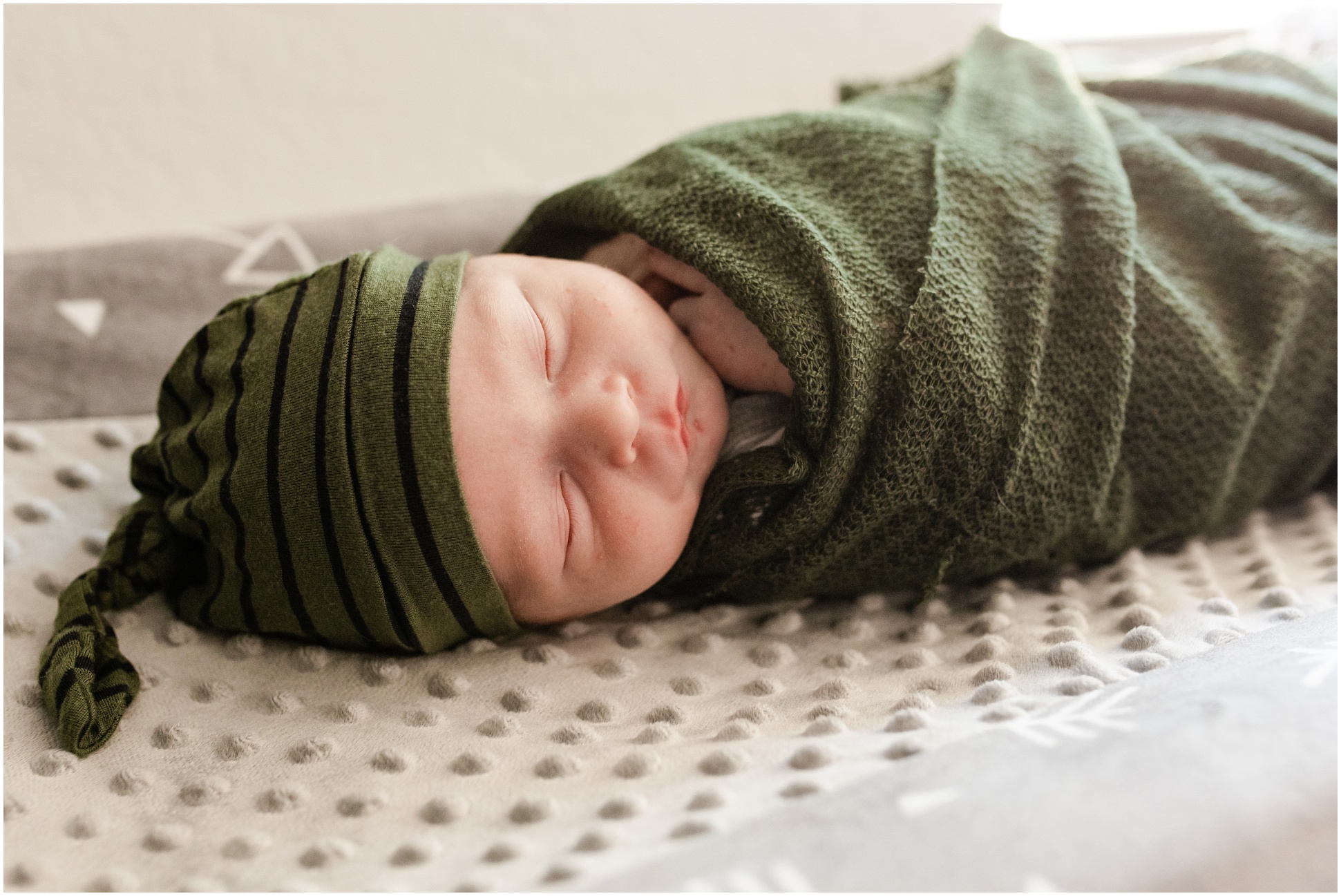 baby resting in army green swaddle ad green and black night cap on grey changing table