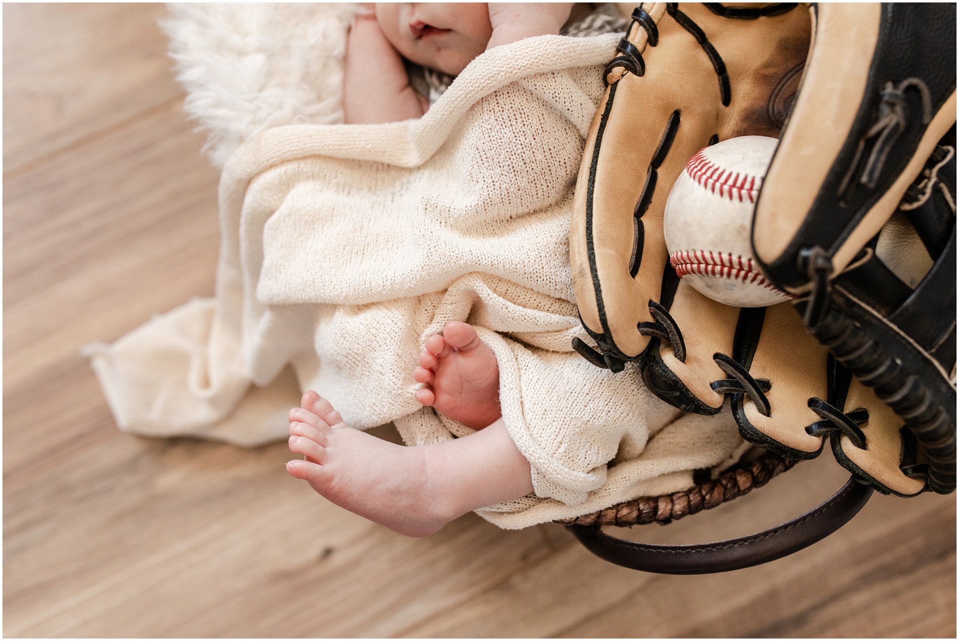 newborn baby feet sticking out of cream colored wrap next to baseball in baseball glove