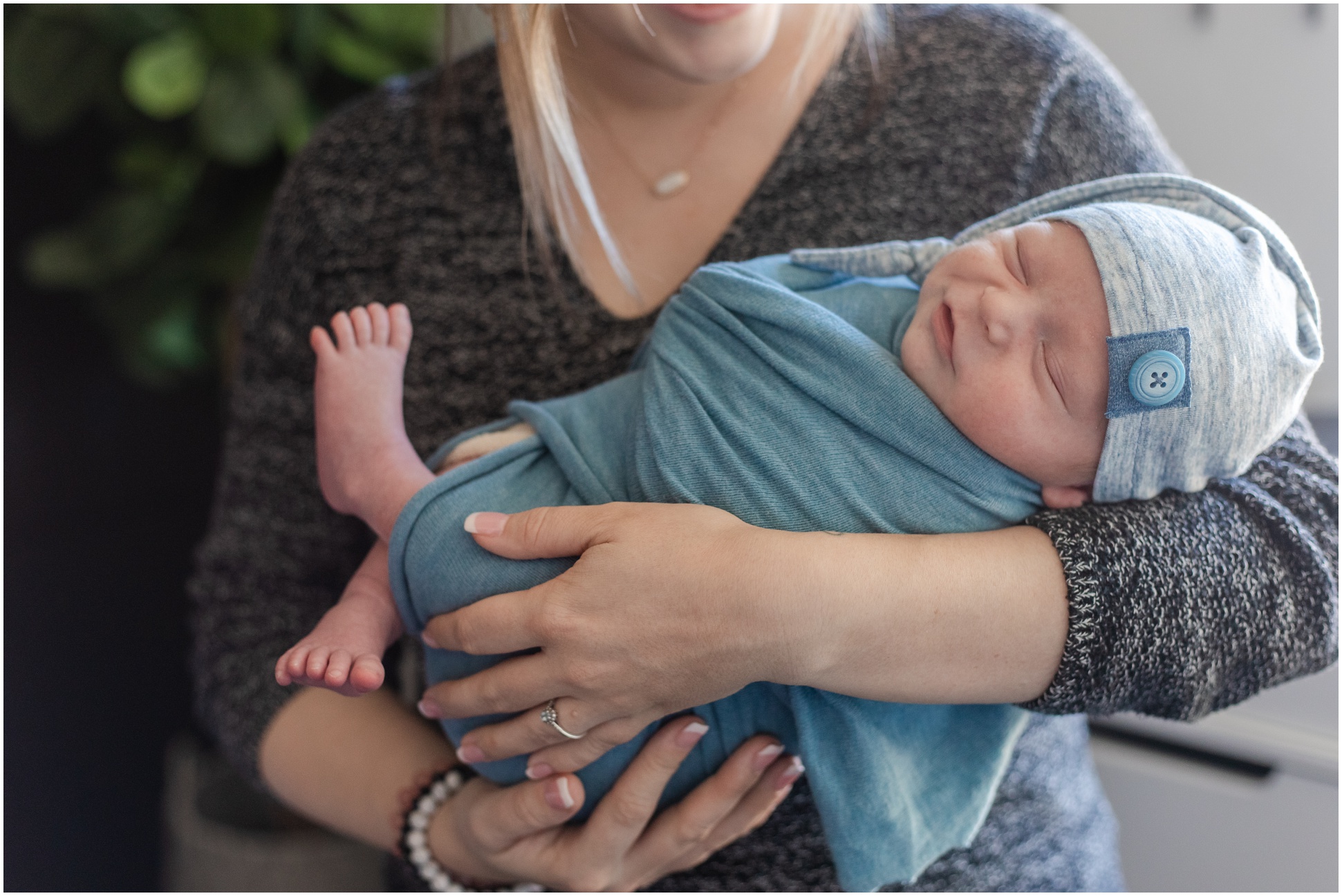mom cradling newborn in grey night cap and blue swaddle with feet sticking out