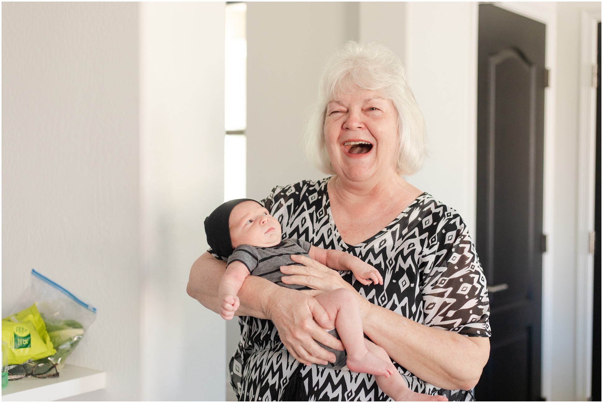 new grandmother laughing at camera while cradling newborn baby 