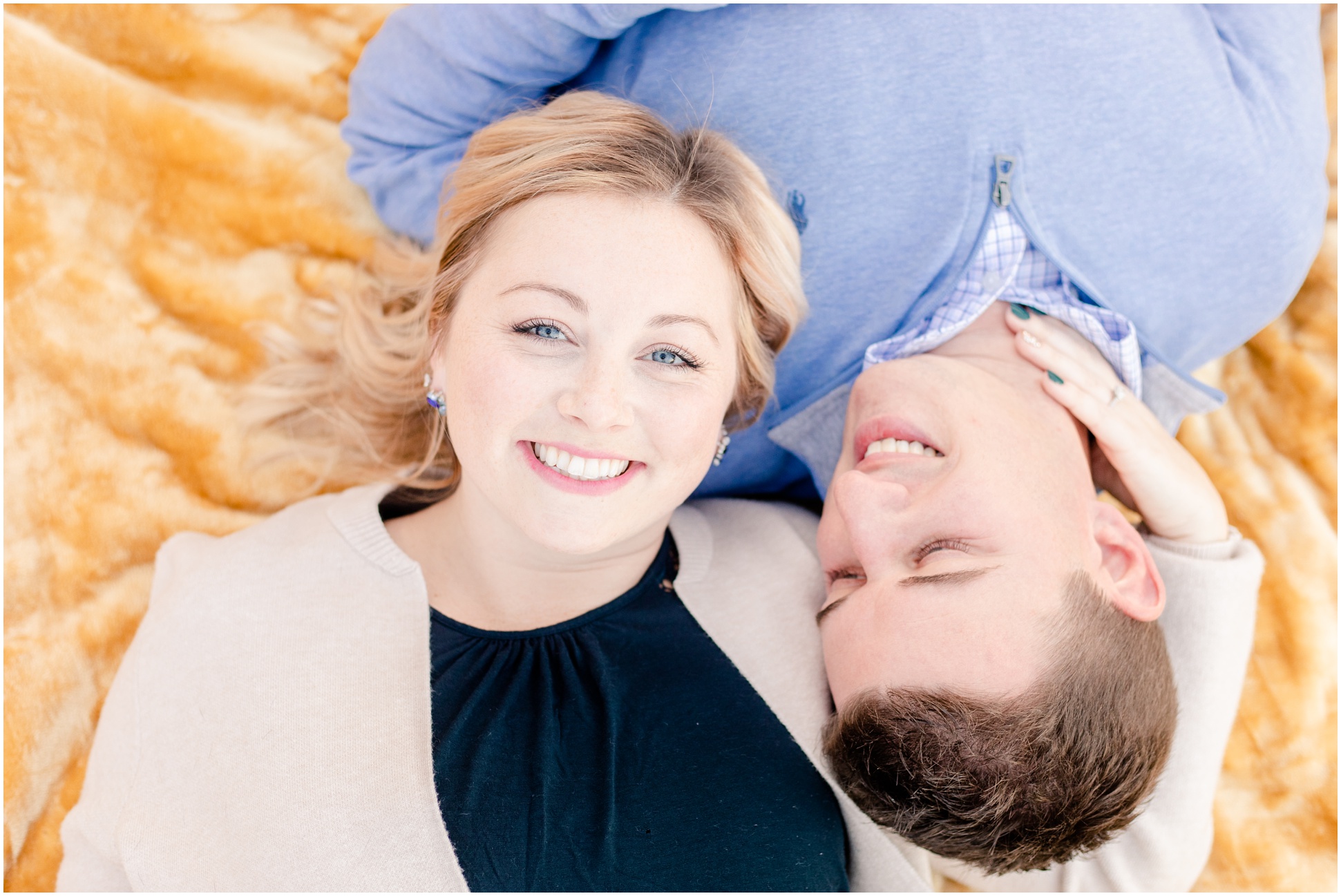 Couple laying on ground in opposite directions with heads touching and smiling at camera