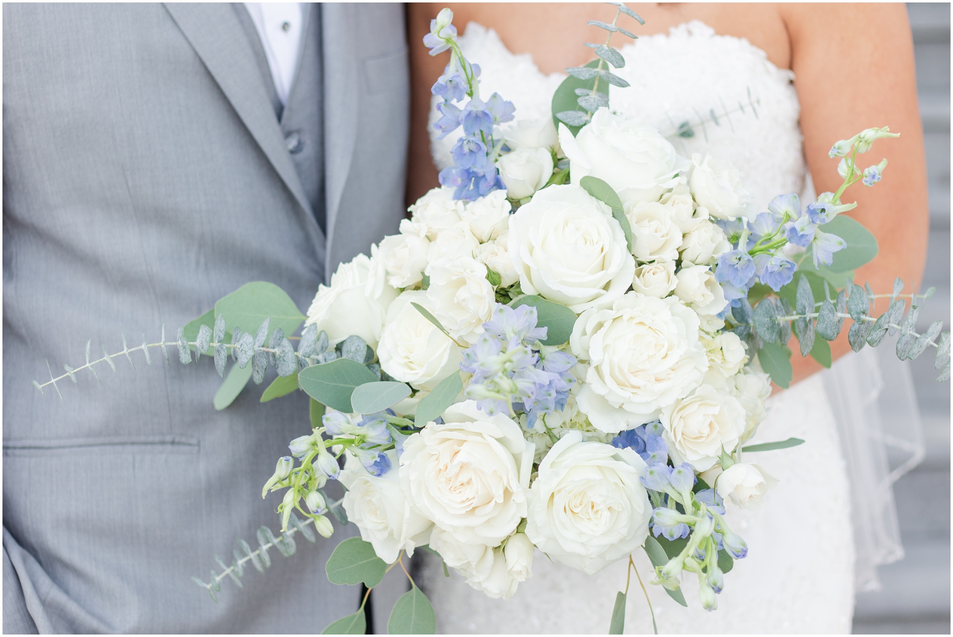 Horizontal Close up of bridal bouquet with white roses, sage stems, and blue snap dragons