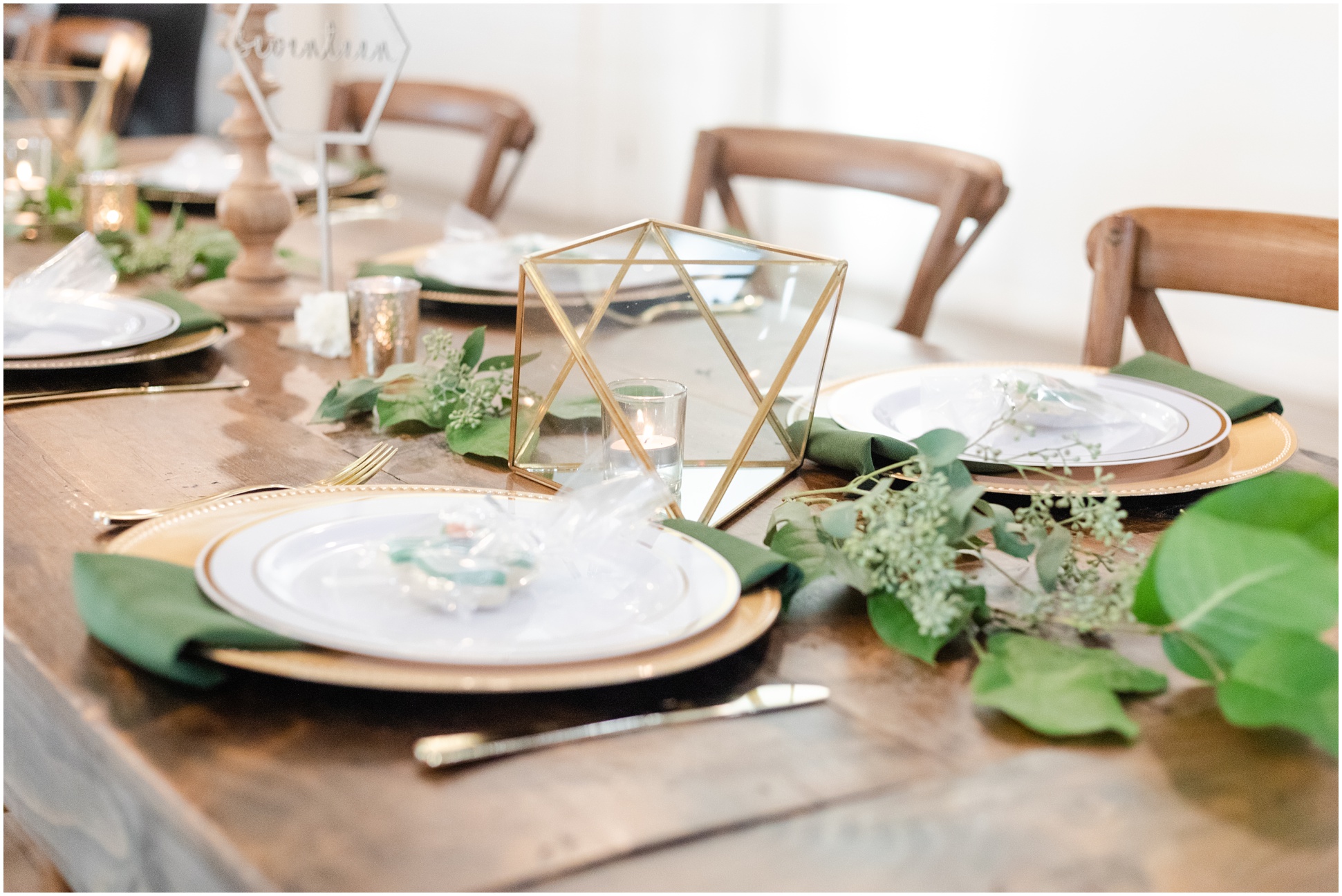 Wedding reception table with white and gold table with green vines in center and geometric table piece with candle in it