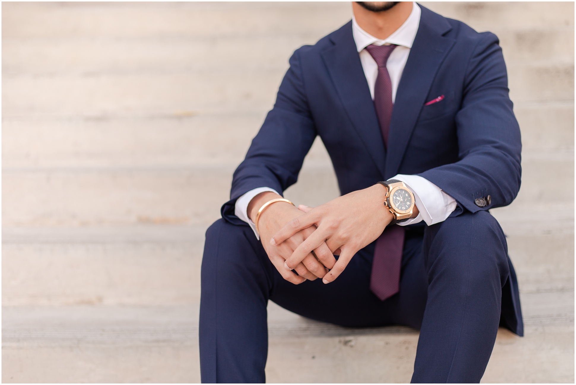 College student sitting on stairs in navy blue suit and gold watch 
