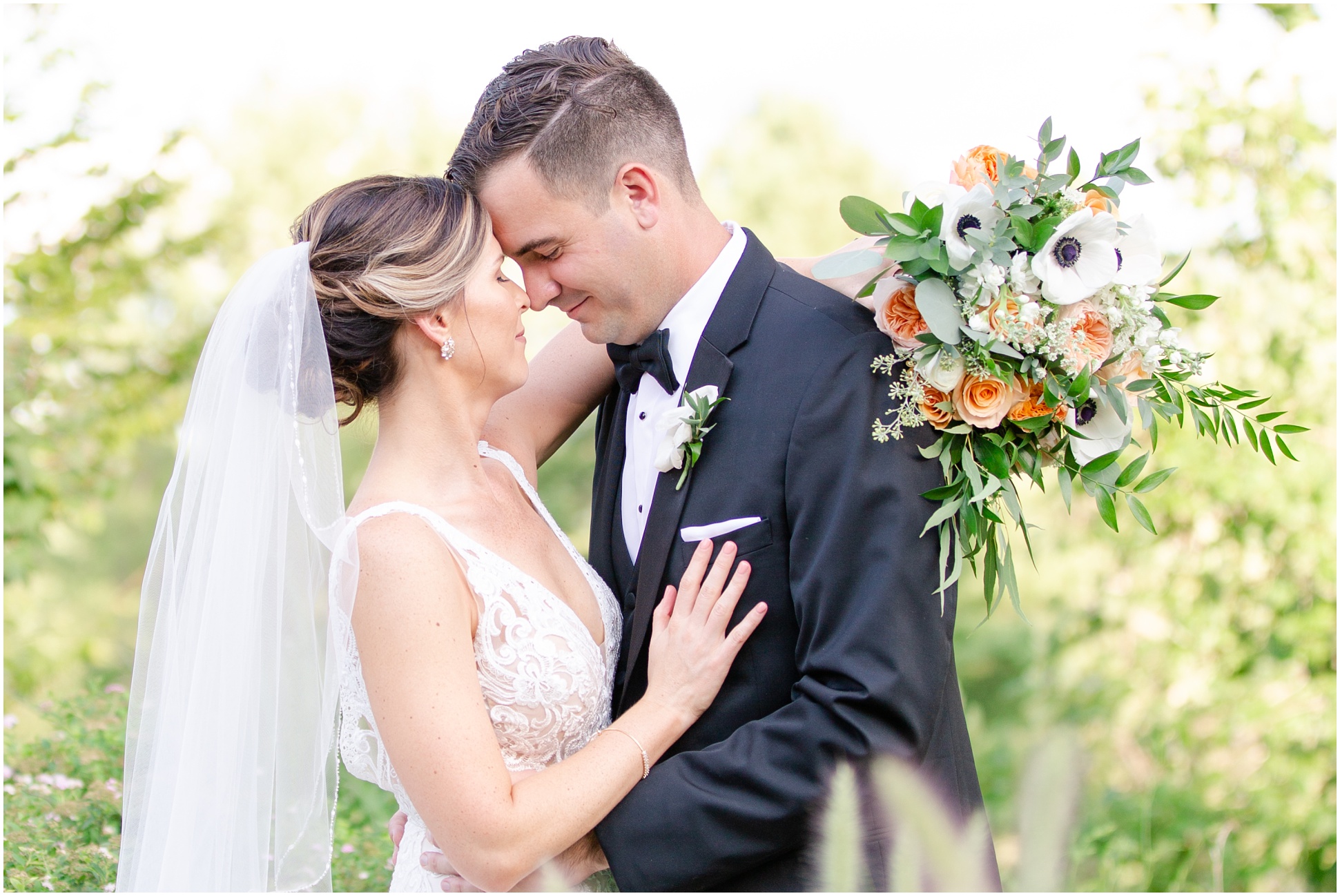 bide wrapping arm holding bouquet around groom while touching foreheads 