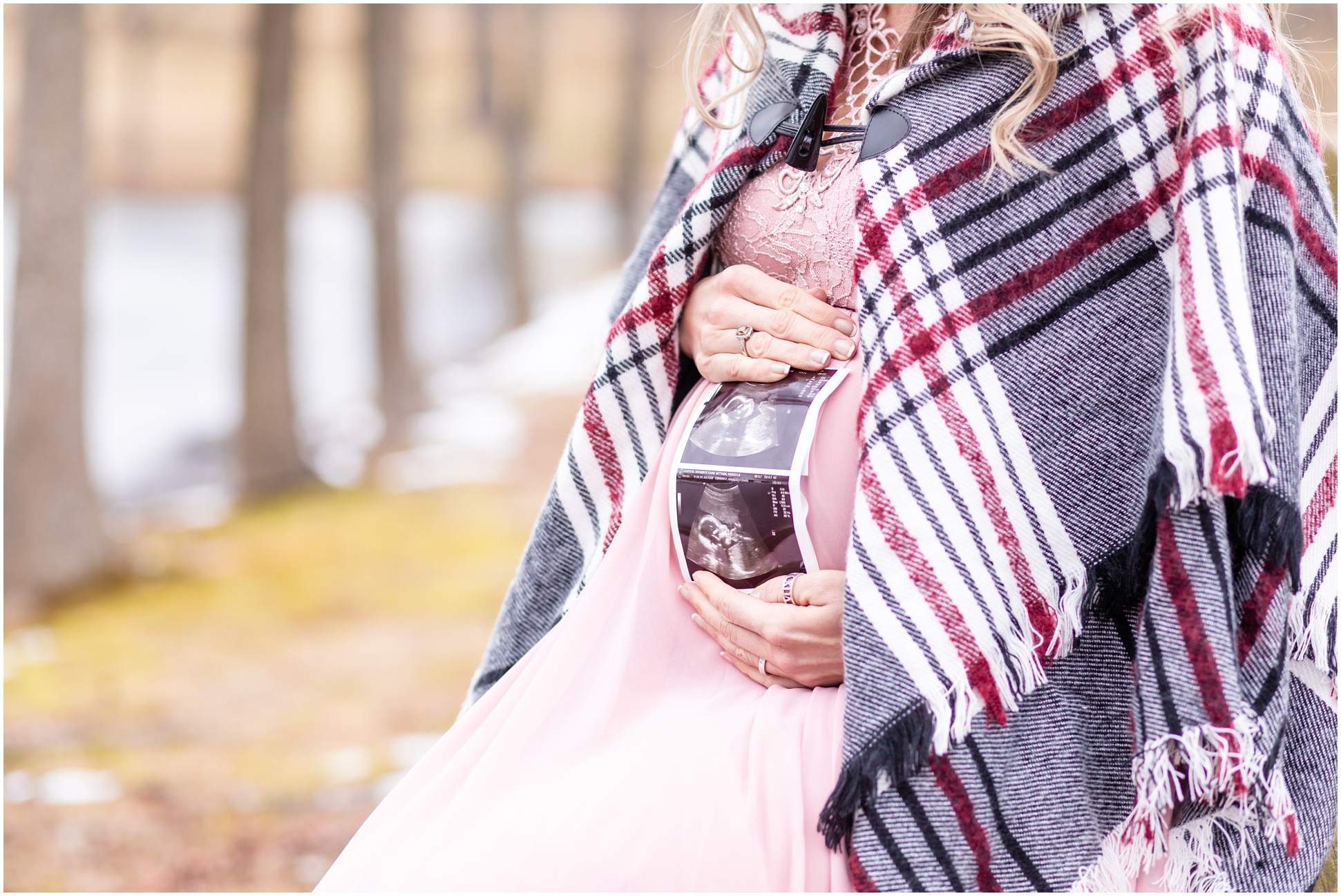 woman holding sonogram to baby bump in light pink dress