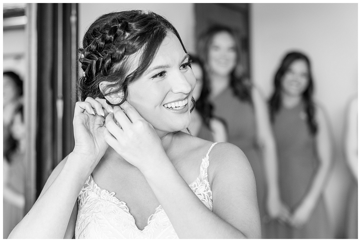bride placing earrings with bridesmaids surrounding her - black and white photo