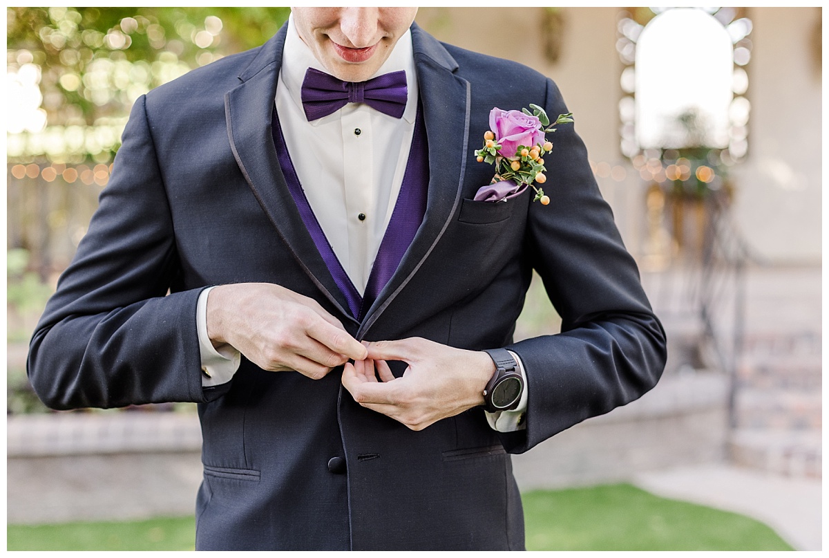 Groom buttoning jacket with purple bowtie