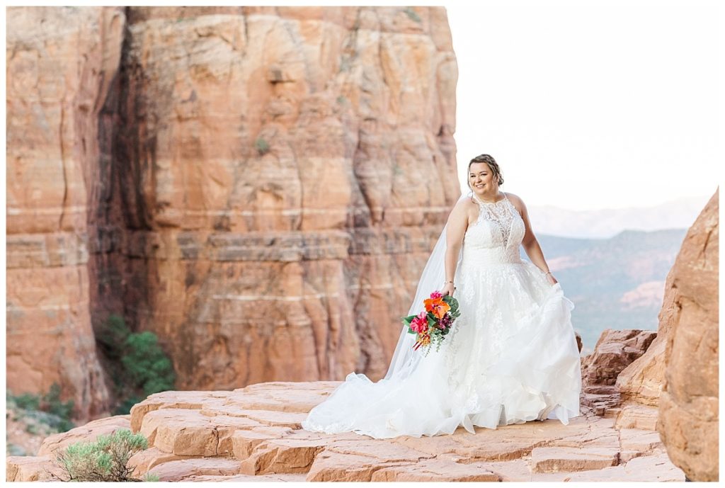 Bride twirling wedding gown while holding bright vibrant bouquet of flowers on top of Cathedral Rock in Sedona, Arizona.