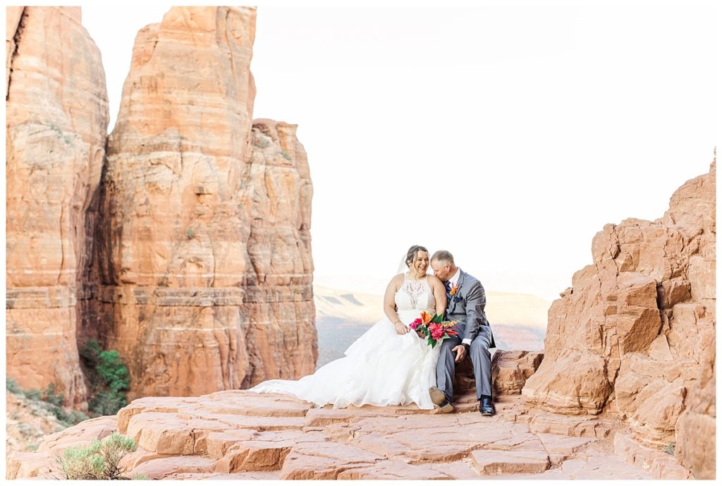 Groom kissing his wife's shoulder sitting at the top of Cathedral Rock in Sedona, Arizona 
