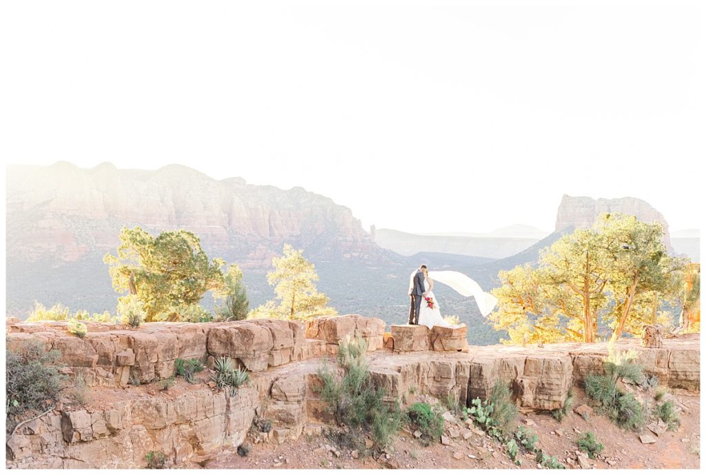 Bride and groom on top of Cathedral Rock kissing as the sun comes up.