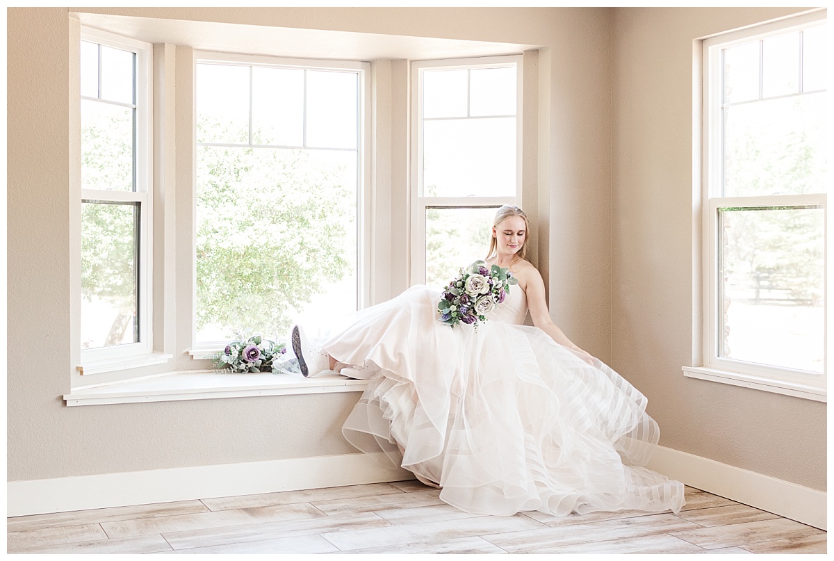 Bride sitting on the window ledge with her bouquet in hand