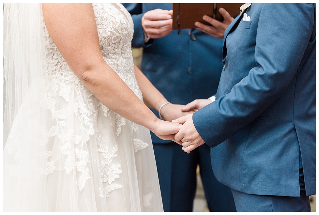 Detail shot of Julia and Andy's hands as they Julia and Andy exchange vows in the enchanting woodland setting of The Stone Mill Inn, York, PA.